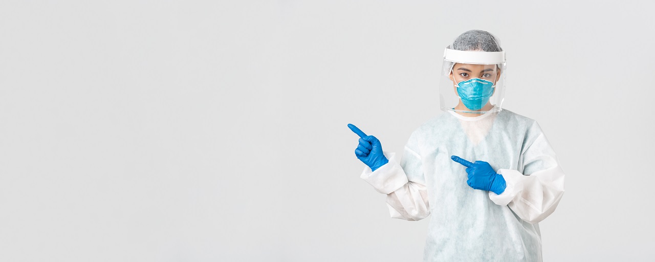 A female operator preparing for a cleanroom environment. She is wearing a white jumpsuit, gloves, and goggles, pointing to her right side